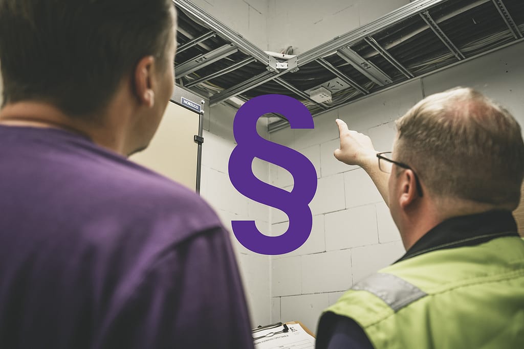 Kata Safetyn Janne ja Joni Rahunen tarkastamassa kiinteistön palokatkoja. Kuvassa kaapelihylly ja keskelle liitetty lakipykälä-symboli