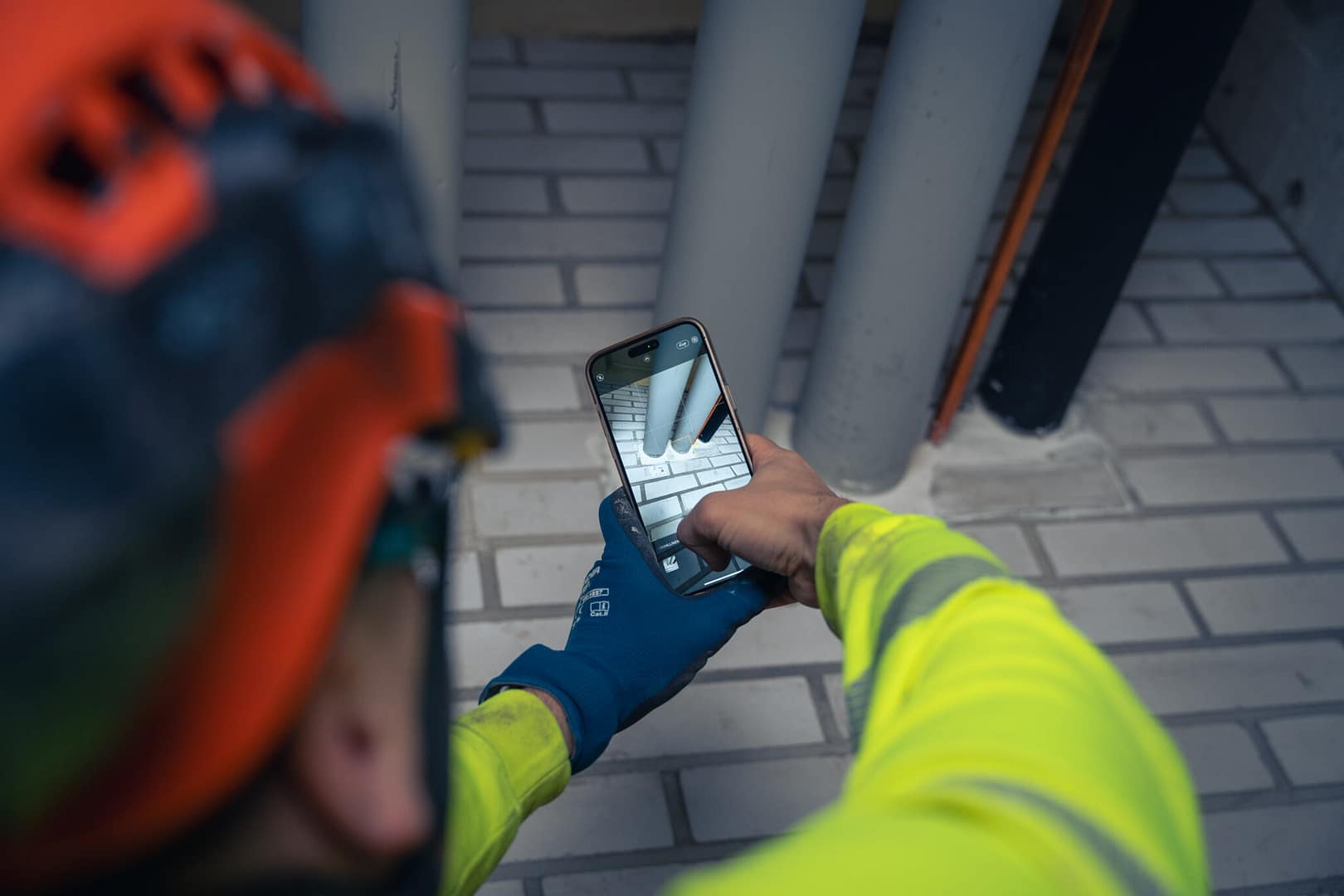 Palokatkojen kartoittaja kuvaamassa matkapuhelimella puutteellista teollisuuden putkiläpiviennin palokatkoa